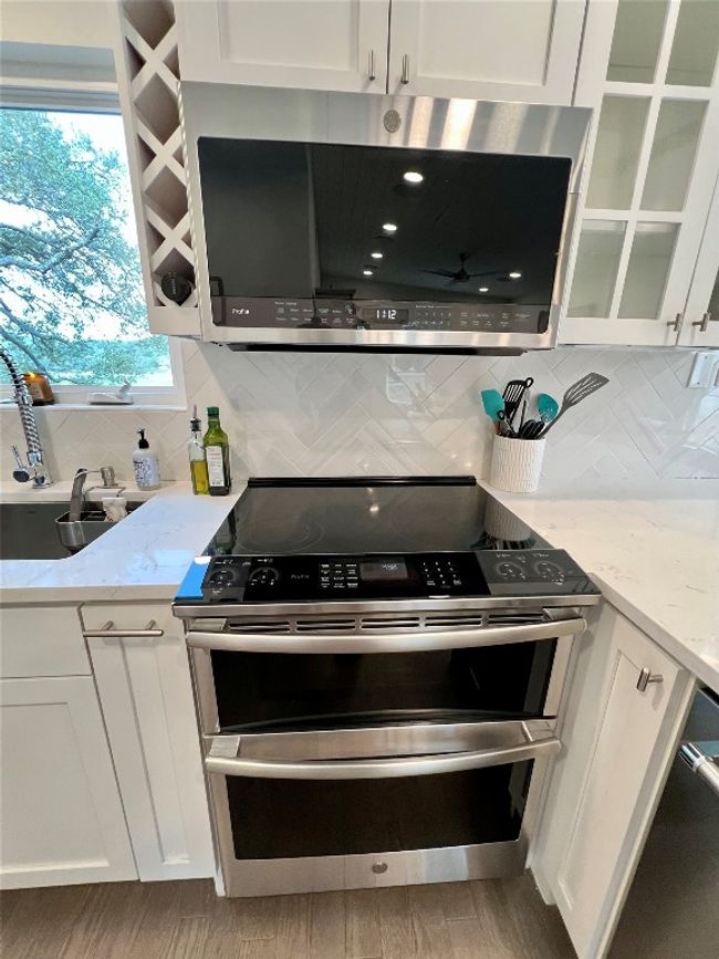 The kitchen features a sleek stainless steel oven and microwave, complemented by a wine rack, under-cabinet lighting, and a chic herringbone backsplash. | Image 8