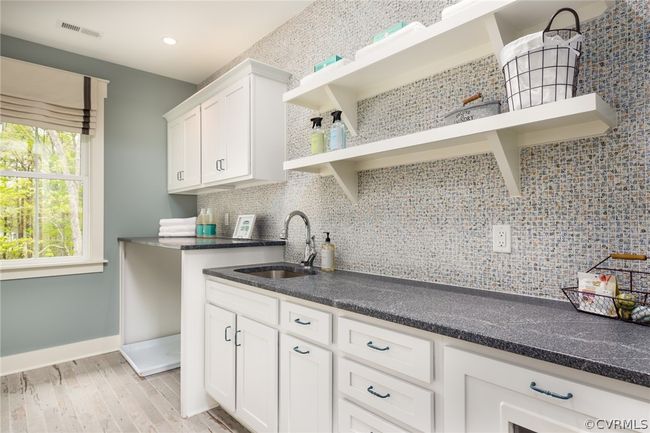 Kitchen featuring tasteful backsplash, light wood-type flooring, dark stone countertops, white cabinets, and sink | Image 8