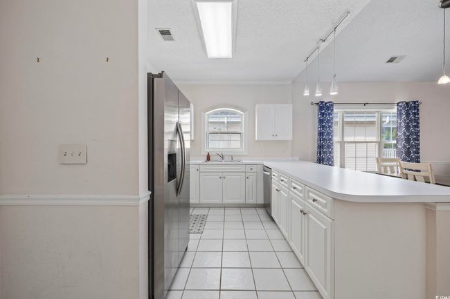Kitchen featuring stainless steel appliances, a textured ceiling, a peninsula, light countertops, and a sink | Image 5