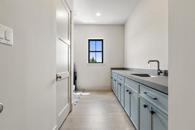 The laundry room is a great working space just off the mud-room tucked between the garage and kitchen. It has a long counter with an undermount sink. Abundant cabinet space and two closets allow for ample storage. A washer and dryer connection are behind the closet on the left. A window allows natural light to fill the space as well. | Image 26