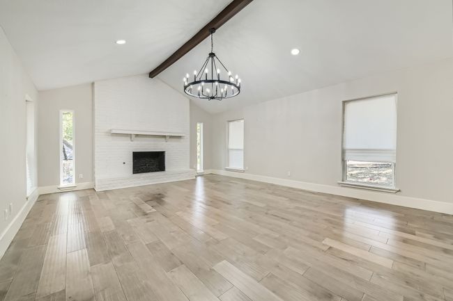 Unfurnished living room with a chandelier, baseboards, vaulted ceiling with beams, and light wood-style floors | Image 5