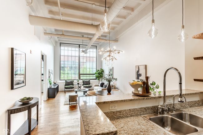 kitchen featuring beam ceiling, light wood-style flooring, a high ceiling, decorative light fixtures, and light stone countertops | Image 14