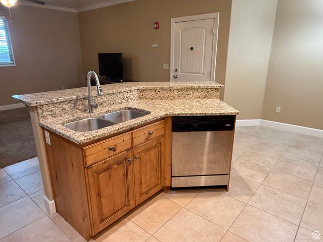 Kitchen featuring stainless steel dishwasher, a sink, ornamental molding, light tile patterned floors, and a center island with sink | Image 7