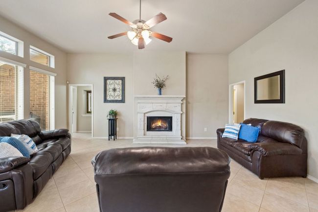Living room with light tile patterned flooring, ceiling fan, and a warm lit fireplace | Image 12
