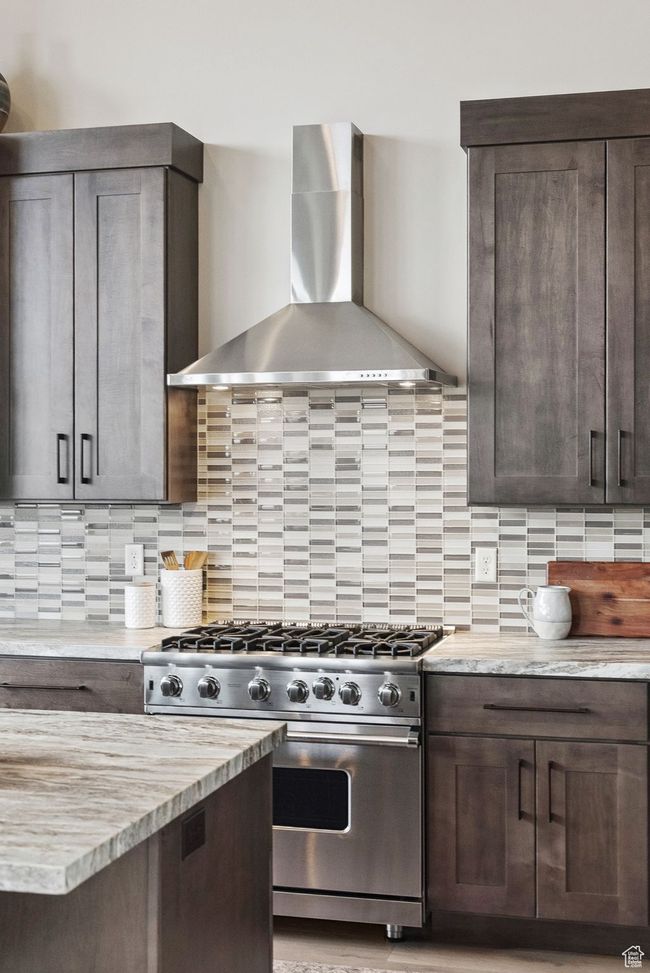 Kitchen featuring wall chimney range hood, stainless steel stove, dark brown cabinetry, and backsplash | Image 22