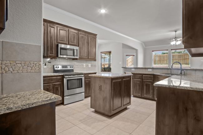 Kitchen featuring crown molding, light stone countertops, a sink, appliances with stainless steel finishes, and a wealth of natural light | Image 9