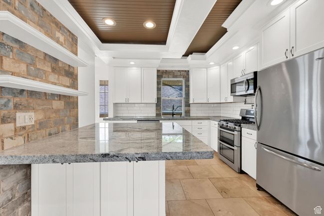 Kitchen with tasteful backsplash, a sink, a tray ceiling, stainless steel appliances, and a peninsula | Image 9