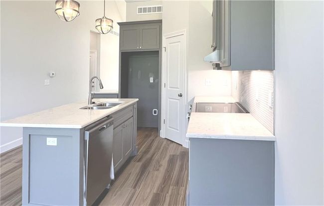 Kitchen featuring gray cabinets, wood finished floors, dishwasher, a center island with sink, and decorative light fixtures | Image 19