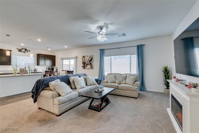 Living area with a ceiling fan, recessed lighting, a glass covered fireplace, and visible vents | Image 8
