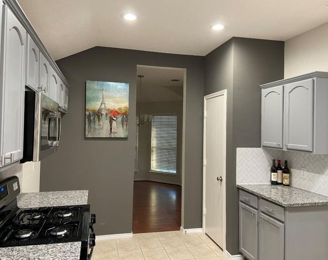 Kitchen featuring gas stove, gray cabinets, backsplash, light tile patterned floors, and stainless steel microwave | Image 9