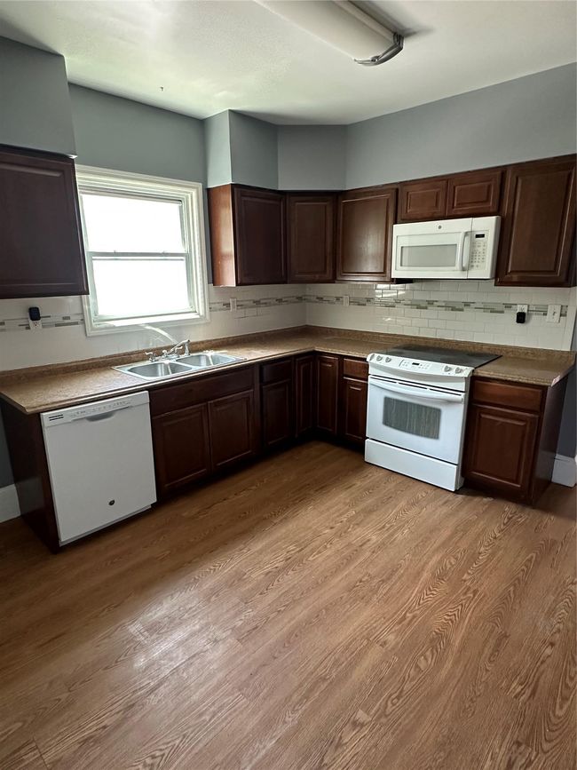 Kitchen featuring white appliances, light wood-style flooring, backsplash, dark countertops, and dark brown cabinets | Image 5