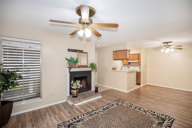 This cozy living space features laminate flooring, a brick fireplace, and ceiling fans. It opens to a kitchen area with wooden cabinets and a light, neutral color scheme, providing a warm and inviting atmosphere. | Image 11