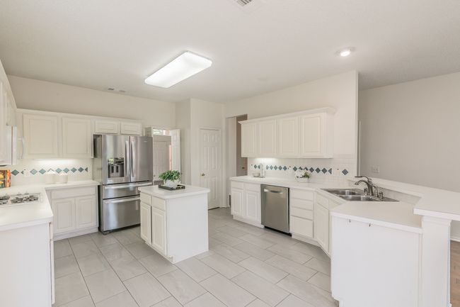 Kitchen with backsplash, light countertops, a sink, a peninsula, and appliances with stainless steel finishes | Image 35