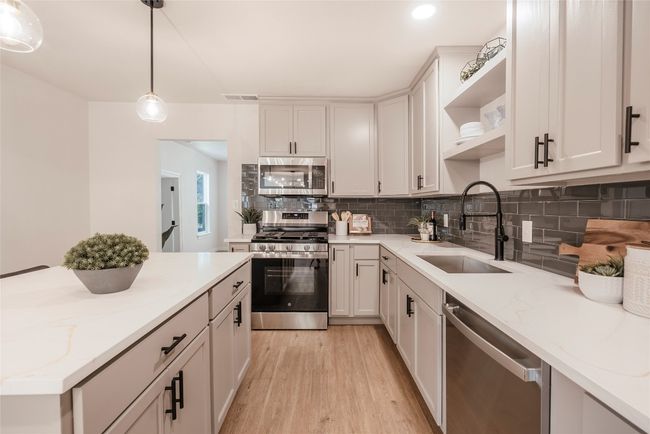 Kitchen featuring appliances with stainless steel finishes, open shelves, backsplash, light wood finished floors, and decorative light fixtures | Image 12