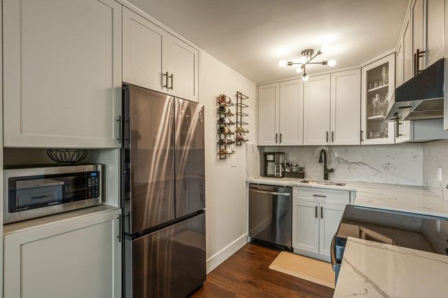 Kitchen with stainless steel appliances, range hood, dark wood-style floors, light stone counters, and glass insert cabinets | Image 16