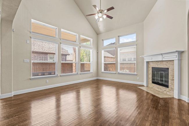 Unfurnished living room featuring ceiling fan, wood finished floors, high vaulted ceiling, a brick fireplace, and baseboards | Image 14