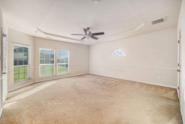 Carpeted empty room with a raised ceiling, a ceiling fan, healthy amount of natural light, and baseboards | Image 29