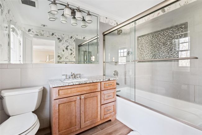 Full bathroom featuring wood finished floors, vanity, bath / shower combo with glass door, toilet, and visible vents | Image 34