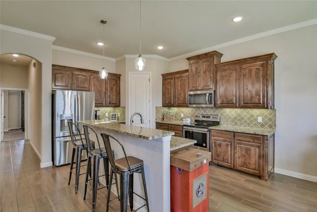Kitchen featuring arched walkways, appliances with stainless steel finishes, wood finished floors and a center island with sink | Image 10