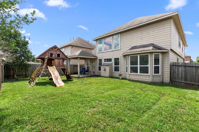 This photo showcases a spacious backyard with a well-maintained lawn, featuring a children's playset with a slide. The back of the house has large windows and a fenced perimeter for privacy, offering a family-friendly outdoor space. | Image 30