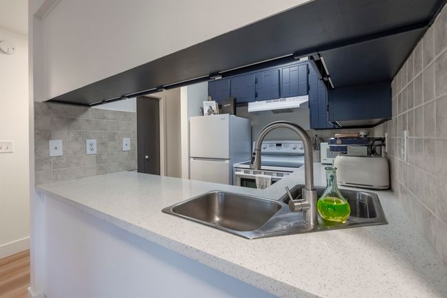 Kitchen featuring white appliances, under cabinet range hood, blue cabinets, wood finished floors, and decorative backsplash | Image 15