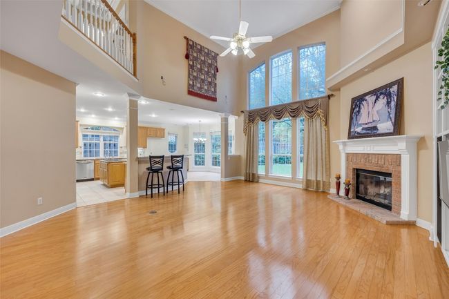Living room featuring decorative columns, ceiling fan, light wood-style flooring, a fireplace, and a towering ceiling | Image 15