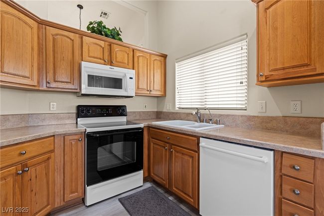 Kitchen with white appliances, light countertops, brown cabinetry, and light wood-style flooring | Image 15