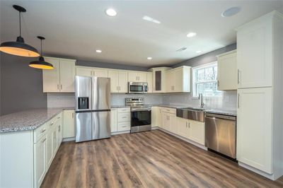 Kitchen with sink, light stone counters, appliances with stainless steel finishes, decorative light fixtures, and dark wood-type flooring | Image 2