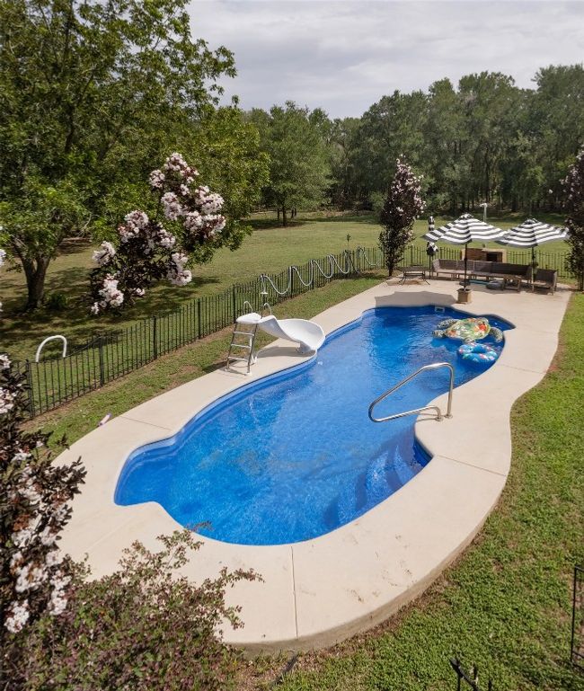 View of swimming pool featuring a fenced backyard, a water slide, a patio, and view of wooded area | Image 36
