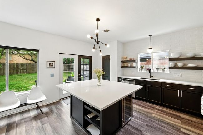 Kitchen with appliances with stainless steel finishes, a sink, wall chimney range hood, open shelves, and dark cabinetry | Image 8
