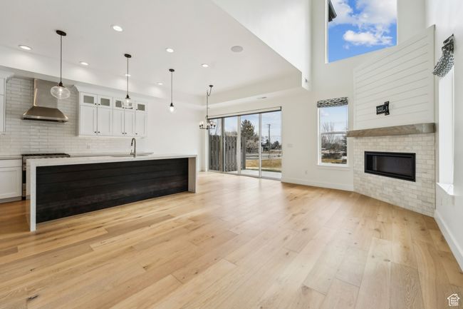 Unfurnished living room with baseboards, recessed lighting, light wood-style flooring, a glass covered fireplace, and a sink | Image 18