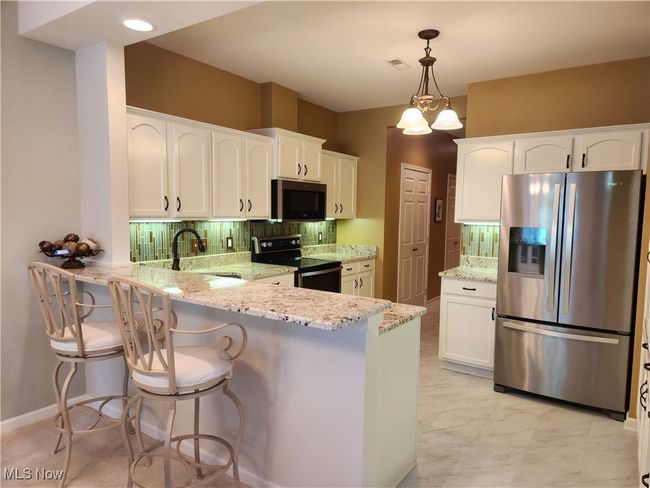 Kitchen with appliances with stainless steel finishes, a peninsula, white cabinetry w/under mount lighting, tasteful backsplash, and light granite counters. | Image 13