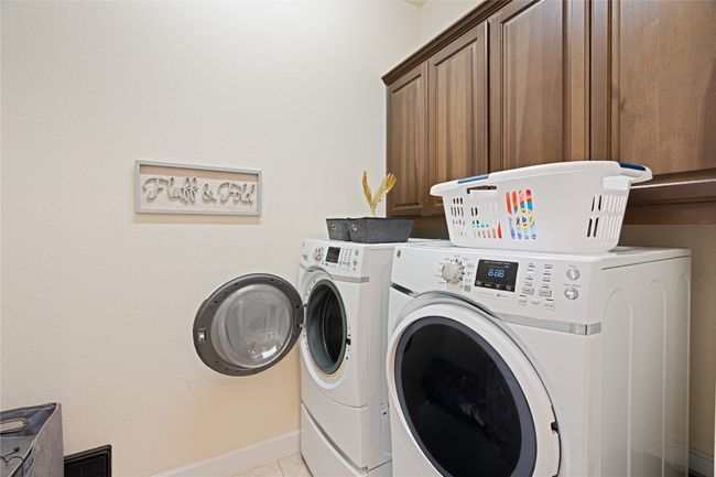 Laundry area featuring cabinet space, washing machine and dryer, and tile patterned flooring | Image 25