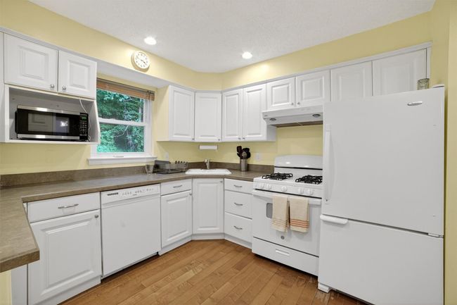 Kitchen with white appliances, under cabinet range hood, white cabinets, and recessed lighting | Image 13