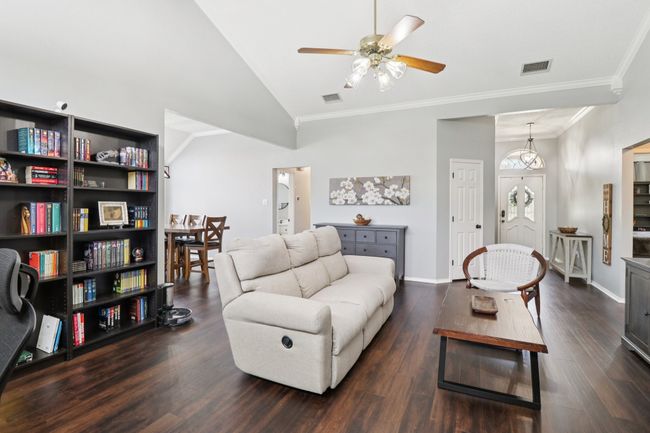 Living room with crown molding, dark wood-style floors, ceiling fan, baseboards, and vaulted ceiling | Image 7