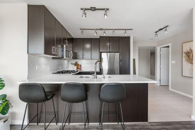 Kitchen featuring stainless steel appliances, a peninsula, a sink, dark brown cabinetry, and a breakfast bar area | Image 6