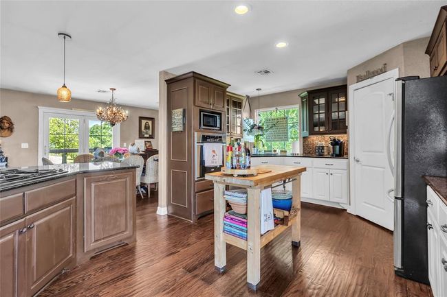 Kitchen featuring appliances with stainless steel finishes, a chandelier, dark wood finished floors, glass insert cabinets, and pendant lighting | Image 13