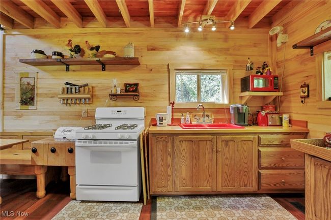 Kitchen with white gas stove, beam ceiling, wooden walls, a sink, and light countertops | Image 12