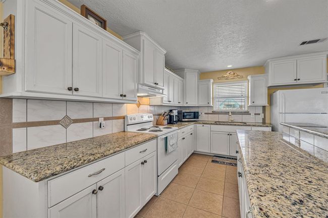 The "galley" style kitchen offers slab granite countertops and custom tile backsplash. | Image 11