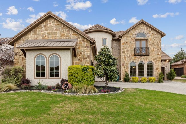 View of front of property featuring a balcony, stone siding, curved driveway, a front yard, and stucco siding | Image 35