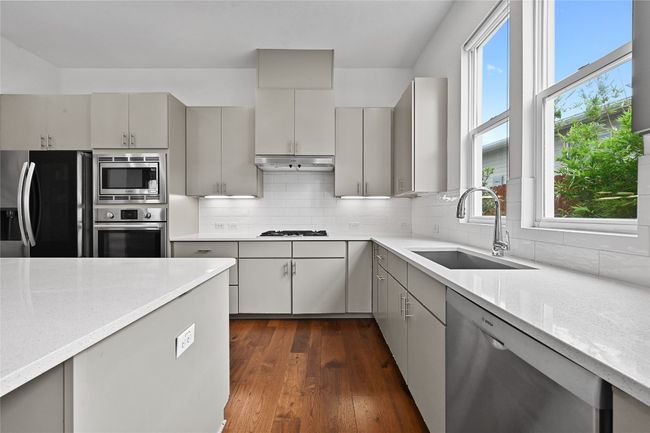 Kitchen with stainless steel appliances, gray cabinets, dark wood finished floors, under cabinet range hood, and decorative backsplash | Image 11