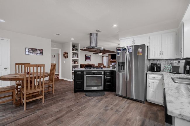 Kitchen with stainless steel appliances, recessed lighting, white cabinetry, dark wood-type flooring, and open floor plan | Image 10