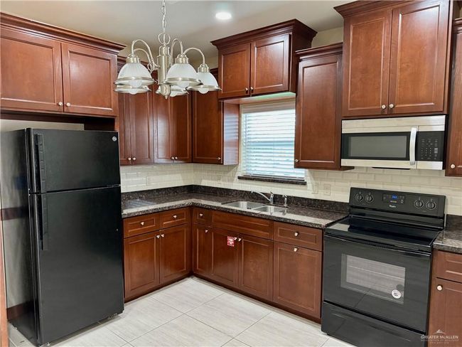 Kitchen with black appliances, light tile patterned floors, tasteful backsplash, and a chandelier | Image 5