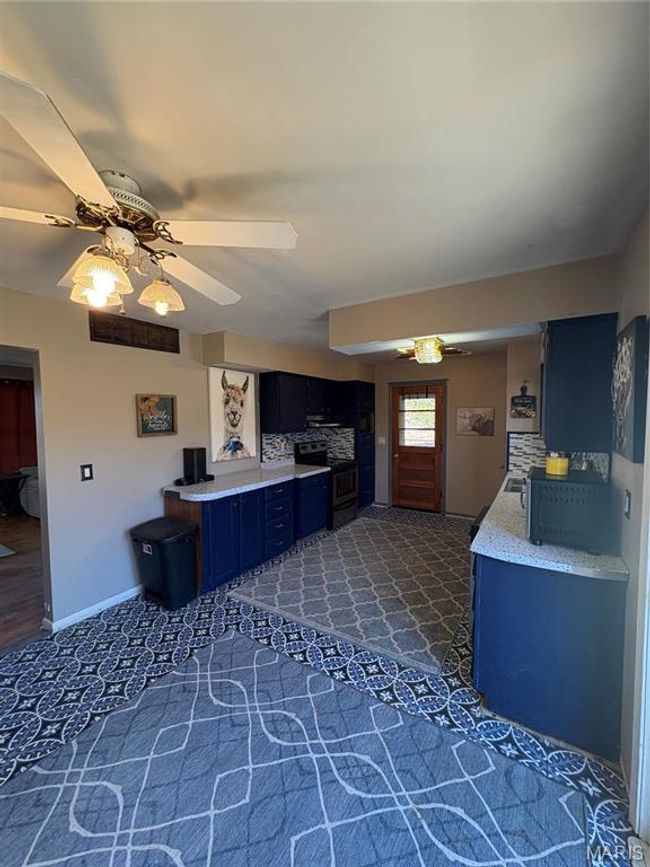 Kitchen with tasteful backsplash, ceiling fan, stove, blue cabinets, and light countertops | Image 11