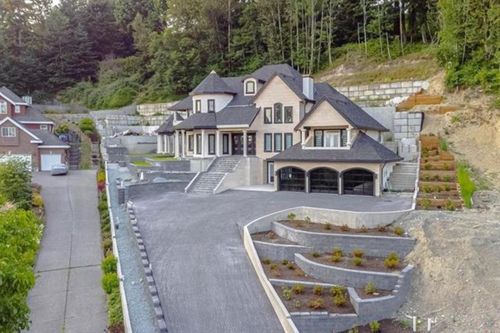 Stately property with extensive retaining walls, multiple tiered landscaping beds, a multi-level concrete driveway, and an attached three-car garage with arched glass doors | Card Image