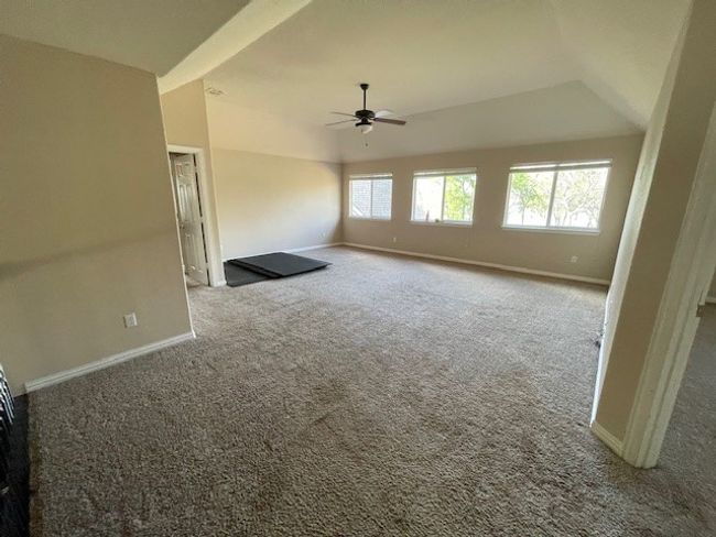 Unfurnished living room featuring ceiling fan, baseboards, carpet flooring, and lofted ceiling | Image 14