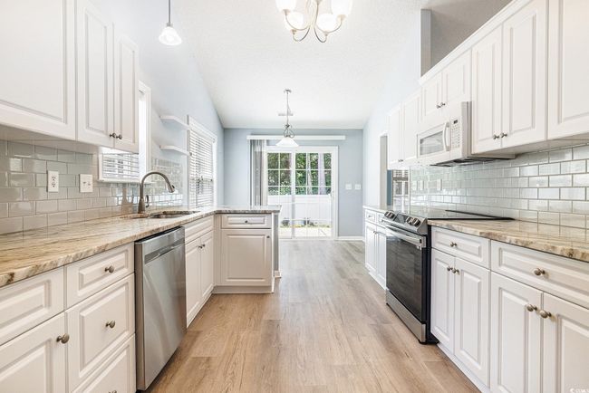 Kitchen with appliances with stainless steel finishes, light wood-type flooring, white cabinetry, vaulted ceiling, and a peninsula | Image 13