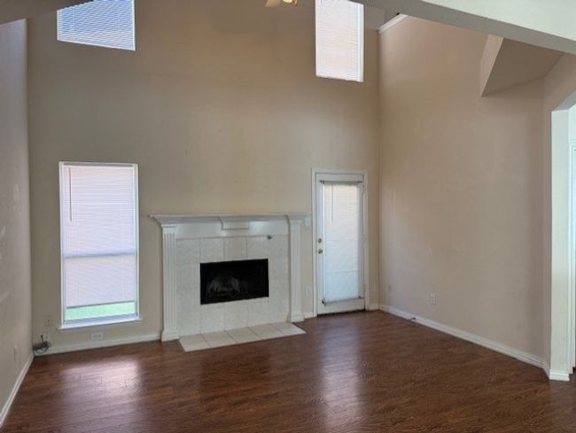 Unfurnished living room with wood finished floors, plenty of natural light, a fireplace, and a high ceiling | Image 4