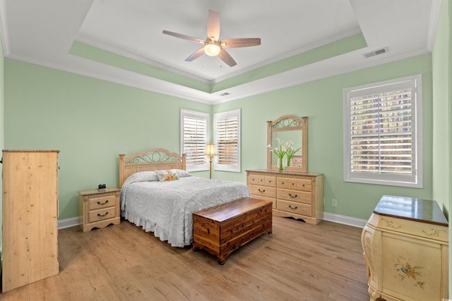 Bedroom with light wood finished floors, baseboards, visible vents, and a raised ceiling | Image 18
