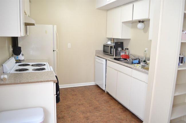 Kitchen with white appliances, white cabinets, under cabinet range hood, light countertops, and dark floors | Image 6